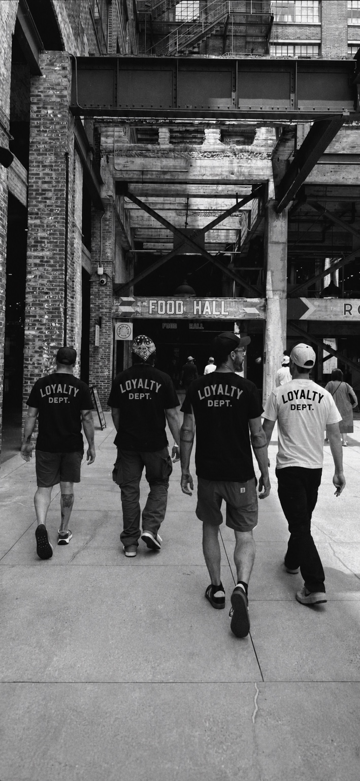 Four individuals wearing Loyalty Dept. tees walking together through an industrial courtyard